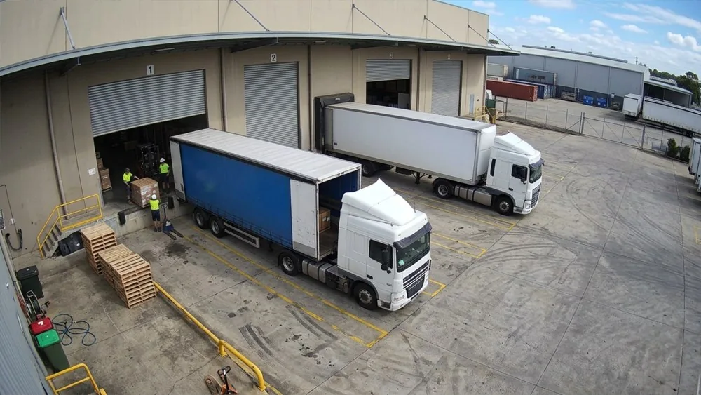 A loading dock camera: two trucks at the bays, pallets on the apron