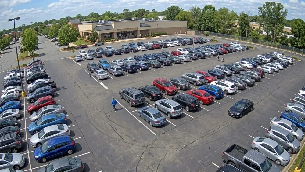A parking lot camera: rows of parked cars with a person walking between them